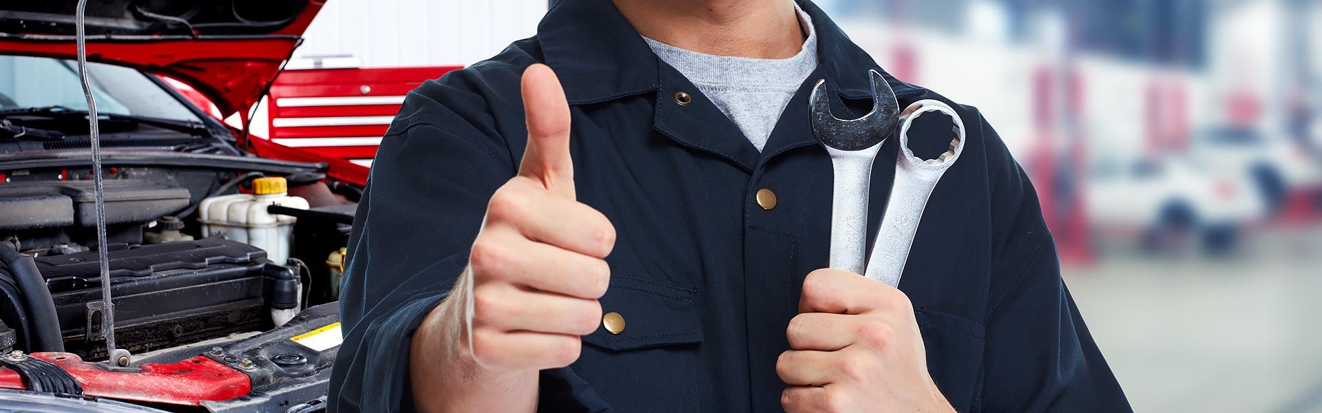 Mechanic holding wrenches and giving a thumbs-up next to an open car hood